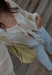 Blusa branca e transparente com decote em babados e cordão; combinada com jeans azul claro; a segurar uma mala amarela texturizada.