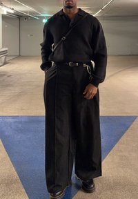 Čierne pletené polo tričko skombinované s nadmerne širokými čiernymi nohavicami. Oblečenie dopĺňa opasok s reťazovým detailom a čierne platformové topánky.