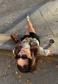 Ținută casual formată dintr-un hanorac gri cu design, fustă mini neagră și adidași maro. Accesorii includ o geantă maro și o cană de cafea.