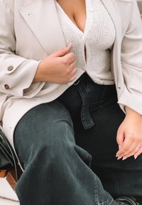 Blazer oversize beige chiaro con bottoni marroni, indossato sopra un cardigan bianco a trama, abbinato a jeans scuri a vita alta.