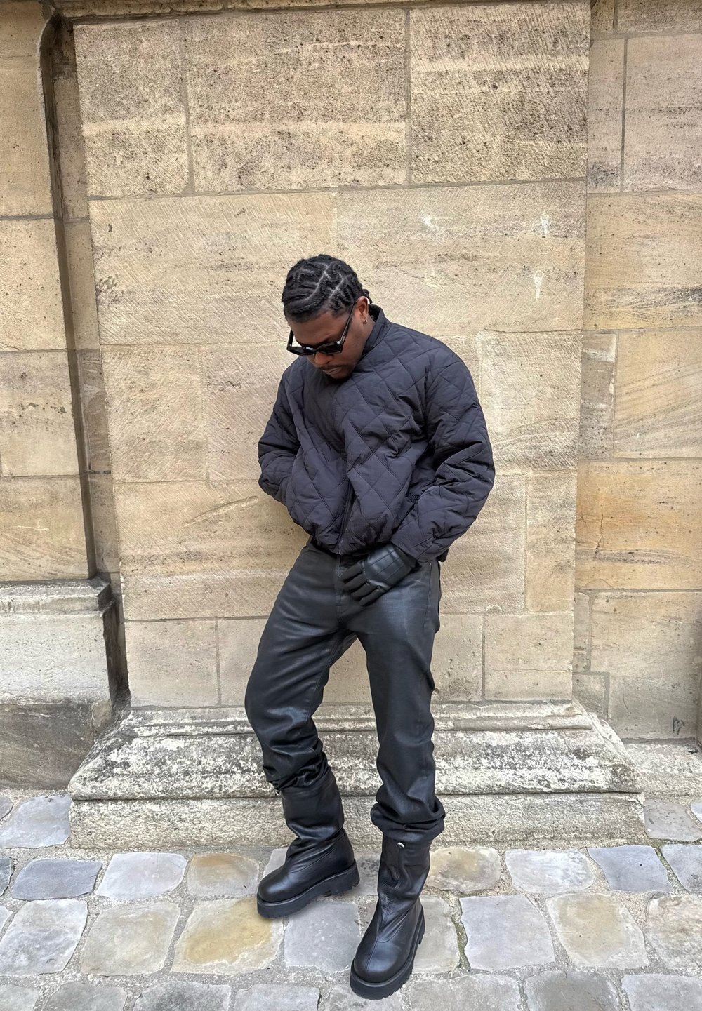 Veste bomber matelassée noire, pantalon en cuir noir et bottes noires montant jusqu'aux genoux. Conçu avec une silhouette ajustée et des matériaux texturés.