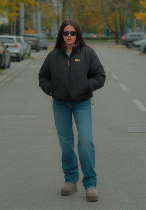 Chaqueta acolchada negra con logo, acentos en rosa, camiseta gris claro, jeans azules y botas de plataforma grises. Conjunto llevado en una calle con coches aparcados.