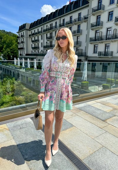 Vestido floral con mangas abullonadas, en colores verde pastel y rosa, con cinturilla ceñida, combinado con un bolso beige y tacones nude puntiagudos.