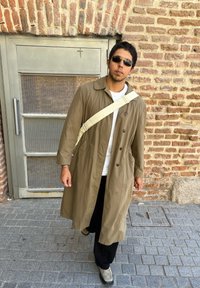 Ελιά-πράσινο παλτό μέχρι το γόνατο με γιακά και δύο πλευρικές τσέπες; φορεμένο πάνω από λευκό πουκάμισο και μαύρο παντελόνι; κρέμα-χρωματιστή τσάντα χιαστί.