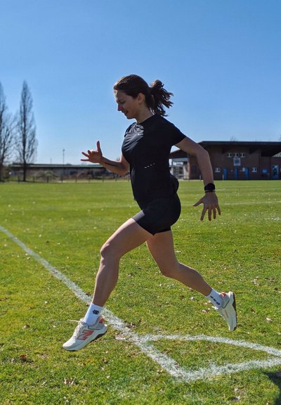 Pantalones cortos deportivos negros y camiseta, zapatillas de correr blancas con acentos rojos, sobre hierba verde, en un entorno al aire libre bajo un cielo azul claro.