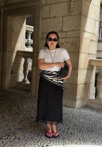 Gonna nera maxi con bordo in pizzo, t-shirt bianca, scialle a fantasia zebratica e pochette nera. Infradito rosse. Occhiali da sole e sfondo in pietra.