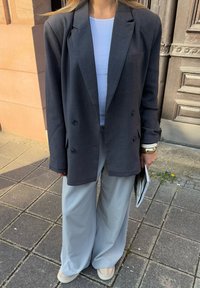 Czarna, ciemnoszara marynarka dwurzędowa o luźnym kroju, zestawiona z jasnoszarymi spodniami o szerokich nogawkach. Marynarka ma duże czarne guziki i klapy.