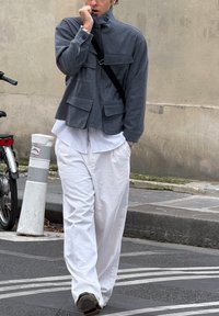 Hall, kraega jope mitme ees taskuga, kantud üle valge särgi. Lahtised valged püksid. Mustad jalanõud. Vabaaja linnakeskkond.