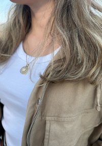 Jacket castanho com fecho de correr sobre uma t-shirt branca de malha canelada, cabelo com luzes loiras claras, textura suave, sem padrões, joalharia mínima.