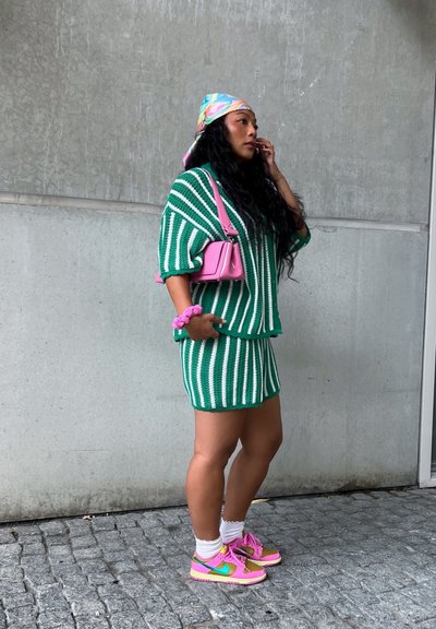 Conjunto de dos piezas de punto a rayas verdes y blancas, complementado con un bolso rosa y zapatillas de colores. Lleva una banda para la cabeza de color pastel y un scrunchie.