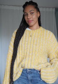 Pull en maille jaune avec une texture côtelée et des manches larges, associé à un jean en denim taille haute. Détails subtils de motif blanc et jaune.