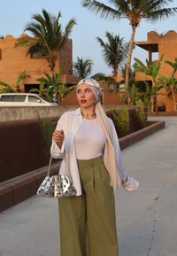 Λευκό πουκάμισο με μακριά μανίκια πάνω από ένα στενό κρεμ τοπ, σε συνδυασμό με ψηλόμεσα ελαιόχρωμα παντελόνια. Συμπληρωμένο με μια ασημένια τσάντα και φουλάρι στο κεφάλι.