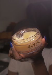 Pro-Collagen rengjøringsbalsam i et klart glass med gullfarge; tykk, kremet tekstur; merket med svart tekst på forsiden.