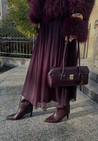 Burgundy veckad kjol, texturerad pälsjacka, matchande väska med guldfärgad hårdvara och spetsiga ankelstövlar. Har rik färg och varierade material.