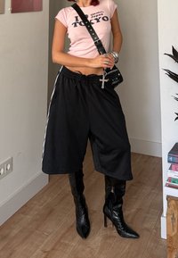 Pantaloni scurți atletici negri cu dungi albe laterale, asortați cu cizme negre stil stiletto până la genunchi. Tricou roz cu imprimeu grafic „I <3 Tokyo”.