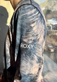 Μακρυμάνικο μπλουζάκι σε μπλε και ροζ σπiral σχέδιο, με λευκό λογότυπο "ROXY" στο μανίκι, φτιαγμένο από λείο, ελαφρύ ύφασμα.