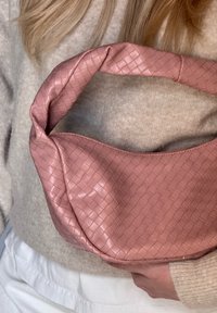 Gewebte rosa Handtasche mit einem dicken, gepolsterten Griff und einer glatten Textur. Die Form ist rund und hat ein entspanntes, schlaffes Design.