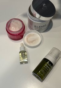 Cztery produkty do pielęgnacji skóry ELEMIS: różowy słoiczek z kremem, biały słoiczek z płatkami do twarzy, szklana buteleczka z pipetą oraz zielona butelka z rozpylaczem.