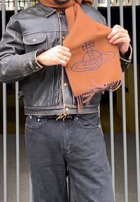 Black leather jacket, black denim trousers, and a brown wool scarf with a navy graphic design. The fringed edges of the scarf provide texture.