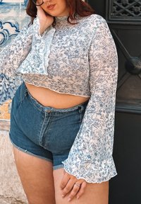 Top corto de encaje floral blanco con estampado de flores azules, mangas con volantes y pantalones cortos de mezclilla de talle alto con bordes deshilachados.