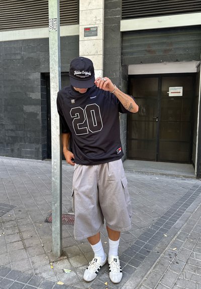 Camiseta deportiva negra con el número 20 en blanco, pantalones cortos de cargo grises, calcetines blancos y zapatillas blancas. Gorra negra con el texto "Adidas Originals".