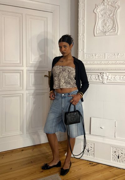 Outfit casual que presenta un top corto de estampado de leopardo, pantalones cortos de denim azul claro tipo Bermuda, zapatos planos negros y un pequeño bolso negro.