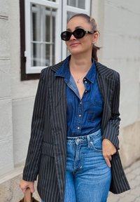 Blazer cu dungi albe și negre peste o cămașă din denim albastru, combinat cu blugi albaștri cu talie înaltă. Accesoriile includ ochelari de soare și un colier.