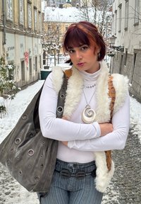 Sac en cuir gris avec découpes circulaires, col roulé blanc, veste en fausse fourrure, pendentif en spirale et collier en forme d'étoile. Jean avec une large ceinture.