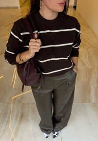 Un pull en tricot rayé marron et blanc, un pantalon olive ajusté, et un sac à cordon bourgogne. Des chaussures à imprimé animal remarquables à bout pointu.