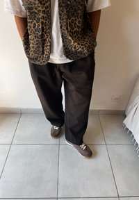 Jopica z leopardjim vzorcem in sprednjima žepoma, bela srajca, črne hlače in rjavi športni čevlji z belimi vezalkami in tekstilnimi detajli.