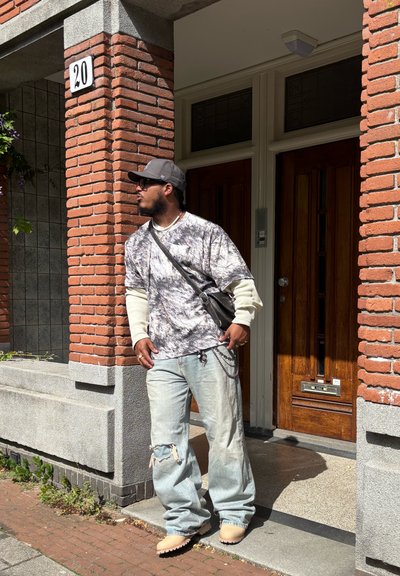 Conjunto casual que incluye una camisa de gran tamaño en gris y blanco jaspeado, jeans desgastados de color azul claro, zapatos tipo slip-on en beige y un bolso negro.