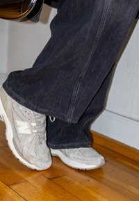 Baskets New Balance gris clair avec des détails en mesh, associées à un jean denim foncé. Présente une coupe décontractée et un design à jambes droites.