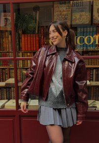 Bordinės odinės striukės su plačiais atlapais, užtrauktuku užsegama, su per didelėmis rankovėmis, derinama su pilku megztiniu ir plisuota suknele.