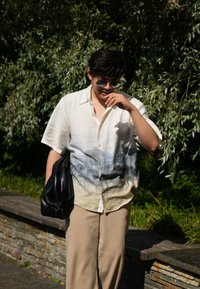 Τιάρι κοντομάνικη με σχέδιο σε κλίμακα μπλε και άσπρου χρώματος, σε συνδυασμό με μπεζ παντελόνι και μαύρη τσάντα. Φοριούνται ασημένιες γυαλιά ηλίου.