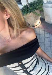 Ριγέ τοπ χωρίς ώμους σε μαύρο και άσπρο χρώμα, με χρυσά κουμπιά. Στο φόντο, πράσινα φυτά σε μια πήλινη γλάστρα.