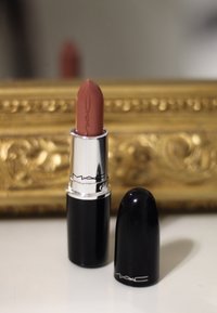 MAC læbestift i en patron-lignende tube med en blank sort ydre og sølvdetaljer. Nuancen er en dæmpet, varm nude.