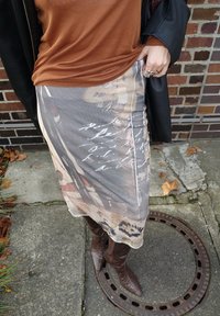 Grey printed skirt with floral and handwritten design, paired with brown leather knee-high boots, and a rust-colored top.