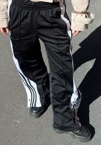 Svart og hvit joggebukse med tapered fit, elastisk midje og sideglidelåser, med markante striper og en jevn tekstur.