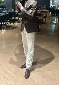 Blazer marron sur une chemise blanche, associé à un pantalon blanc texturé et des mocassins marron foncé, dans un intérieur de restaurant moderne.