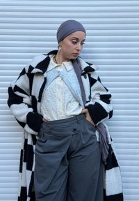 Abrigo largo de tablero de ajedrez en blanco y negro, blusa blanca con textura, pantalones grises con un botón y un hiyab gris. Accesorios mínimos.