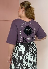 Μωβ υπερμεγέθη μπλούζα με μαύρο ουράνιο γραφικό και κείμενο στην πλάτη, σε συνδυασμό με φούστα ψηλόμεση με μαύρες και λευκές βούλες.