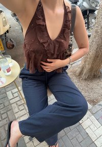 Brun halterneck-top med volanger og subtile pynt, paret med marineblå løstsittende bukser. Svarte sandaler og en liten veske med stropp.