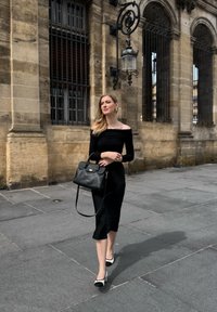 Top off-shoulder nero abbinato a una gonna nera, con una borsa a mano strutturata nera. Presenta tacchi a punta bianchi e neri.