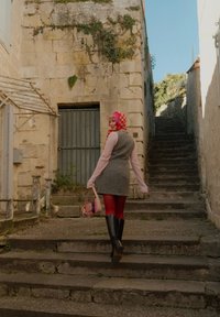 Gråstrikket vest over en rosa langermet topp, røde strømpebukser og svarte høyhælte støvler. Bærende en rosa håndveske på steintrappen.
