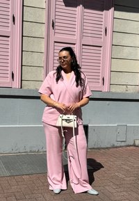 Rosa todelt outfit med en omslagstopp og brede bukser. Tilbehøret inkluderer en lille hvid håndtaske og oversized solbriller.