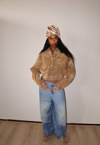 Brązowa, krótka koszula ze sztruksu z guzikiem z przodu i szerokimi rękawami, zestawiona z jasnoniebieskimi, wysokim stanem i szerokimi nogawkami dżinsami. Wzorzysty turban na głowę.