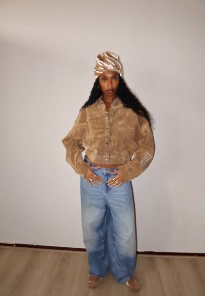 Camisa de pana marrón corta con cierre de botones al frente y mangas anchas, combinada con vaqueros de pierna ancha, tiro alto y azul claro. Pañuelo con estampado en la cabeza.