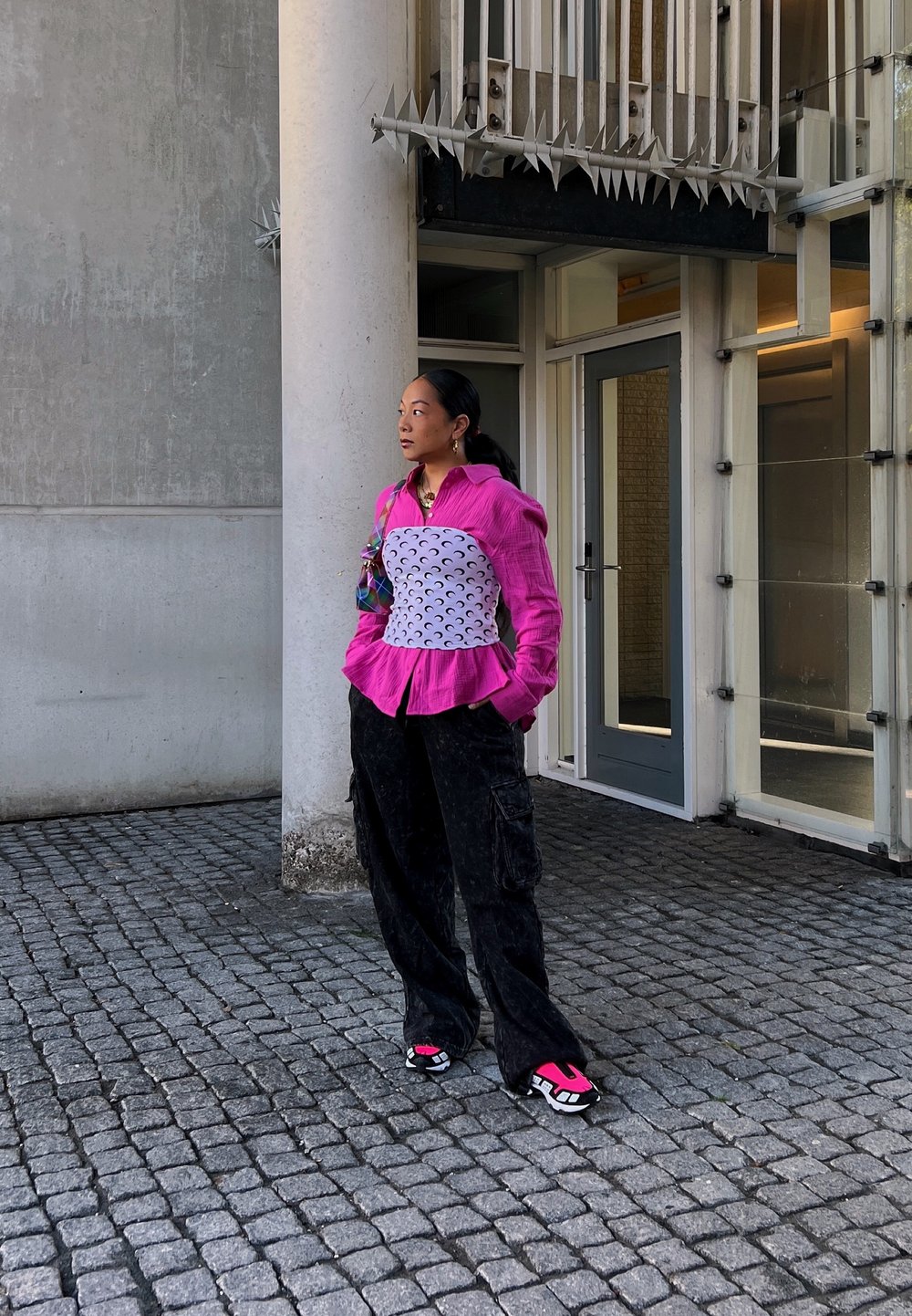 Rózsaszín, texturált blúz peplum fazonnal, fehér testéket felölelő félhold mintákkal, fekete cargo nadrág, és színes sportcipők rózsaszín részletekkel.