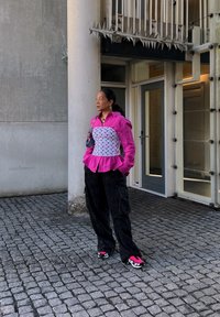 Rózsaszín, texturált blúz peplum fazonnal, fehér testéket felölelő félhold mintákkal, fekete cargo nadrág, és színes sportcipők rózsaszín részletekkel.
