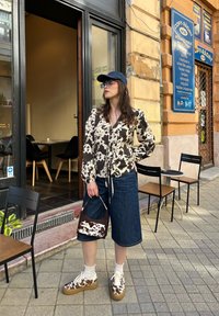Ilga rankovė blouse su rudos ir grietinėlės spalvos karvės raštu, derinama su džinsinėmis kelnių knygelėmis, taškuotais sportbačiais ir derančia rankine, visiškai atsitiktinėje aprangoje.